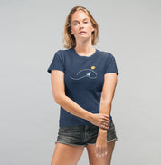 Mulher usando camiseta azul marinho À Beira do Dia da Latitude23, com estampa minimalista de veleiro sob o sol, simbolizando o nascer do dia e o espírito náutico.