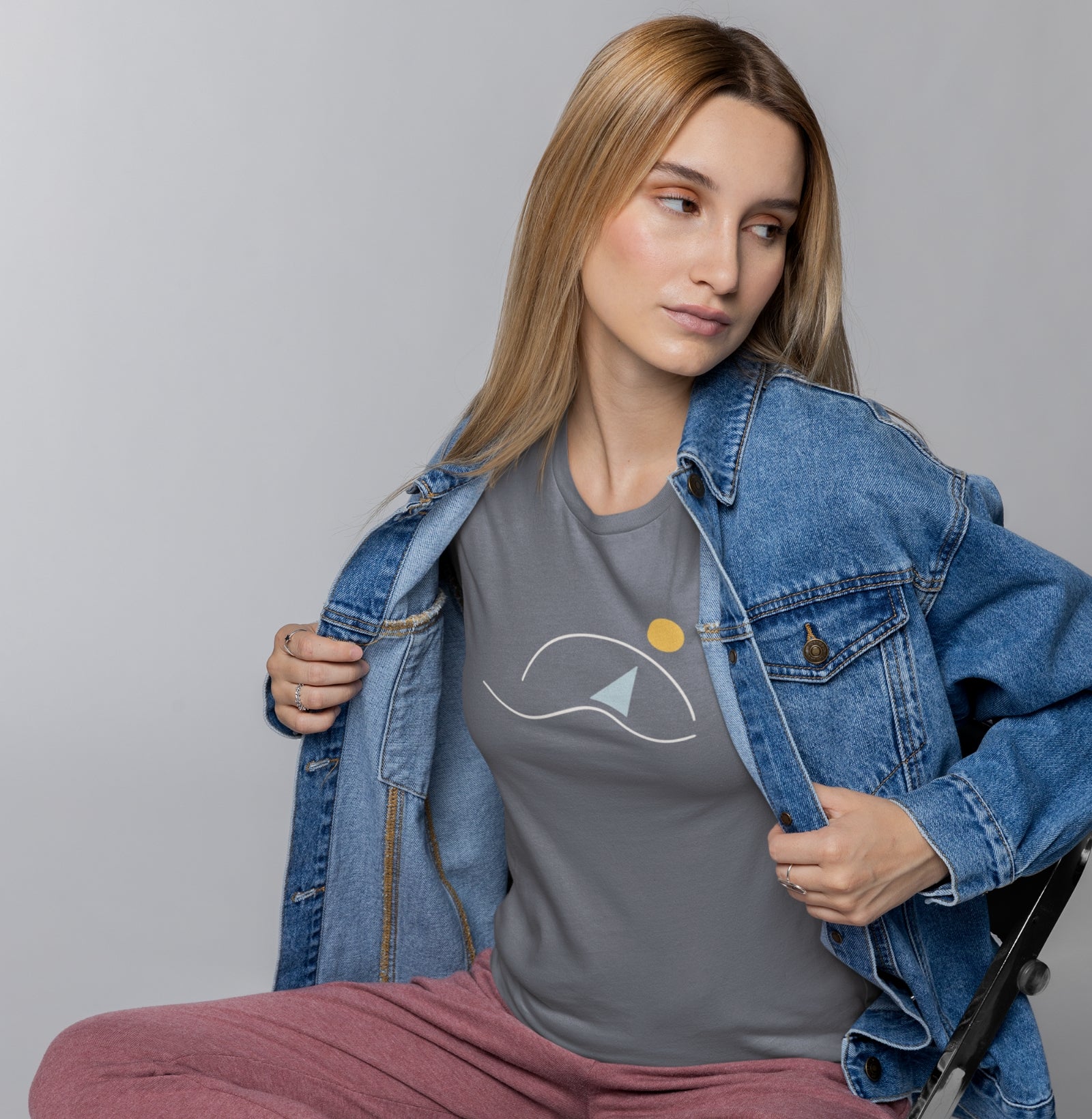 Mulher sentada usando camiseta cinza À Beira do Dia da Latitude23, com estampa de veleiro e sol minimalista, transmitindo leveza e inspiração náutica.