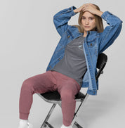 Mulher sentada com jaqueta jeans aberta usando camiseta cinza À Beira do Dia da Latitude23, exibindo estampa minimalista inspirada no horizonte marítimo.