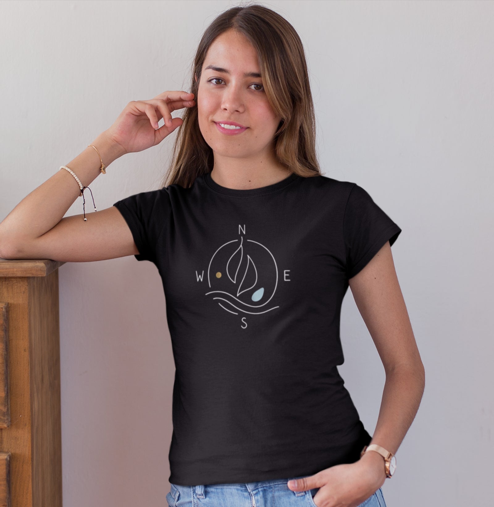 Mulher usando camiseta preta Between Four Winds da Latitude23, com design minimalista de bússola e veleiro em traços finos inspirados no estilo náutico contemporâneo.