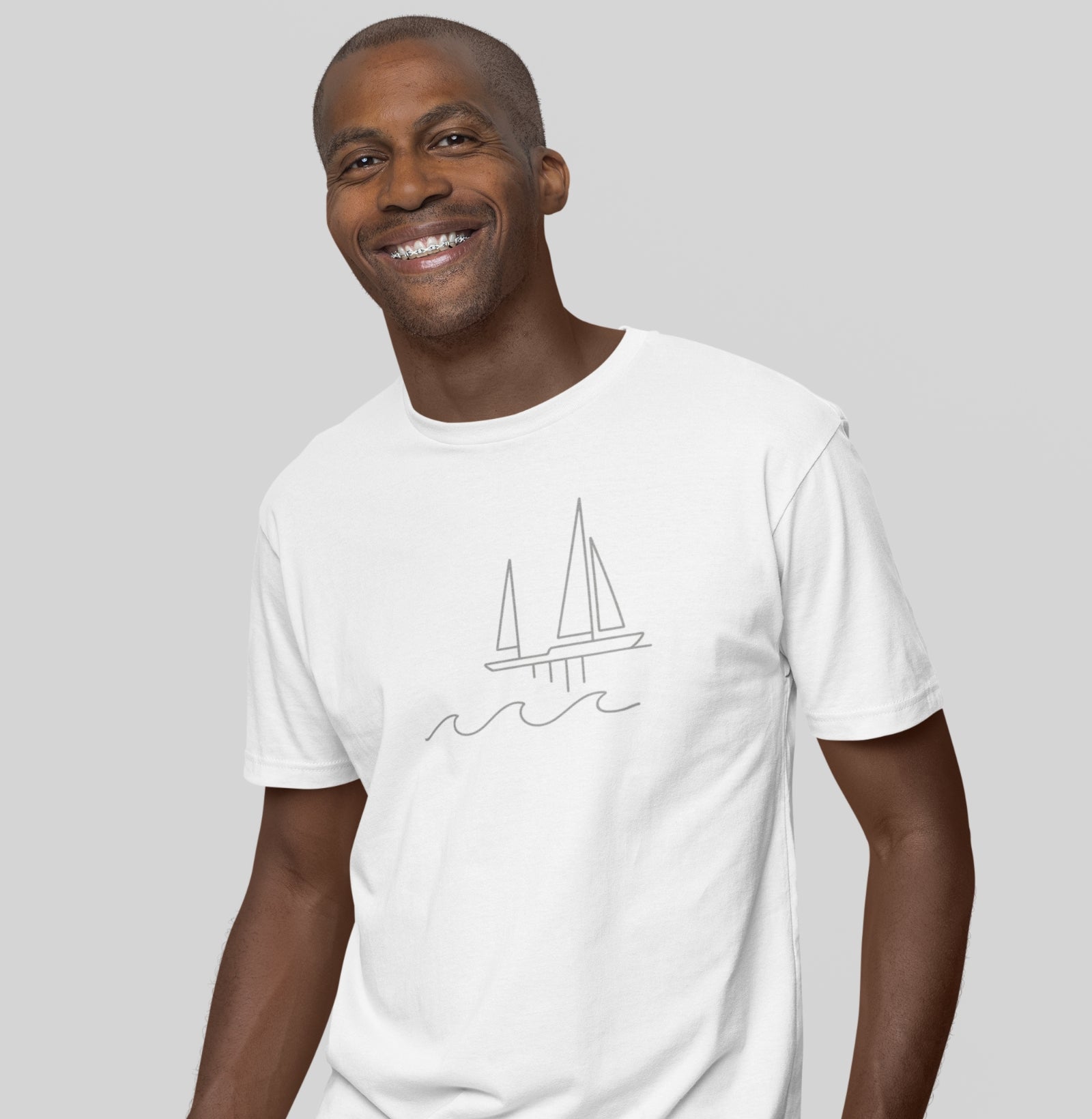 Homem sorrindo usando camiseta branca Between Waves da Latitude23, com estampa minimalista de veleiro sobre ondas, inspirada na tranquilidade do mar.