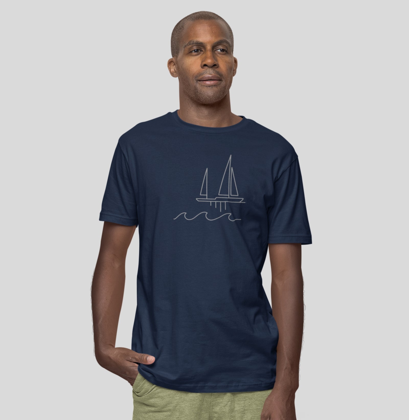 Homem vestindo camiseta azul marinho Between Waves da Latitude23, com estampa minimalista de veleiro e ondas, refletindo elegância e calma náutica.
