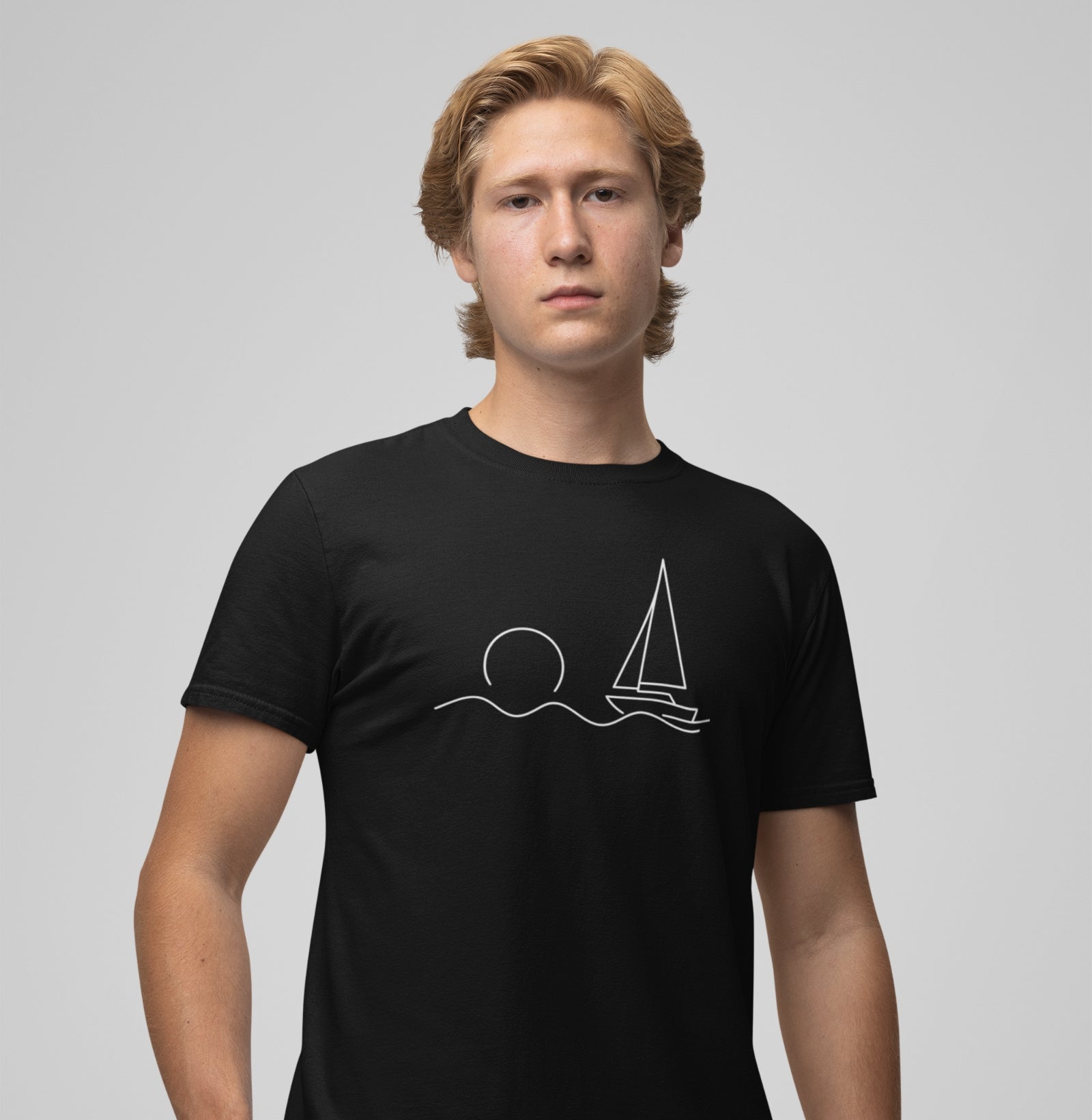 Homem vestindo camiseta preta Beyond the Sail da Latitude23, com estampa de veleiro minimalista sob o sol, simbolizando liberdade e espírito náutico.