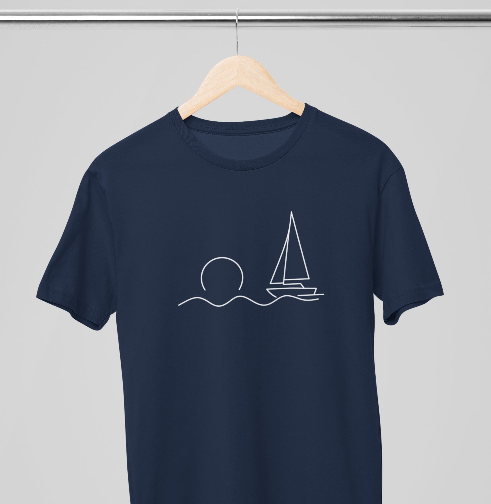 Camiseta azul marinho Beyond the Sail da Latitude23 pendurada em cabide, com estampa minimalista de veleiro e sol representando calma e elegância náutica.
