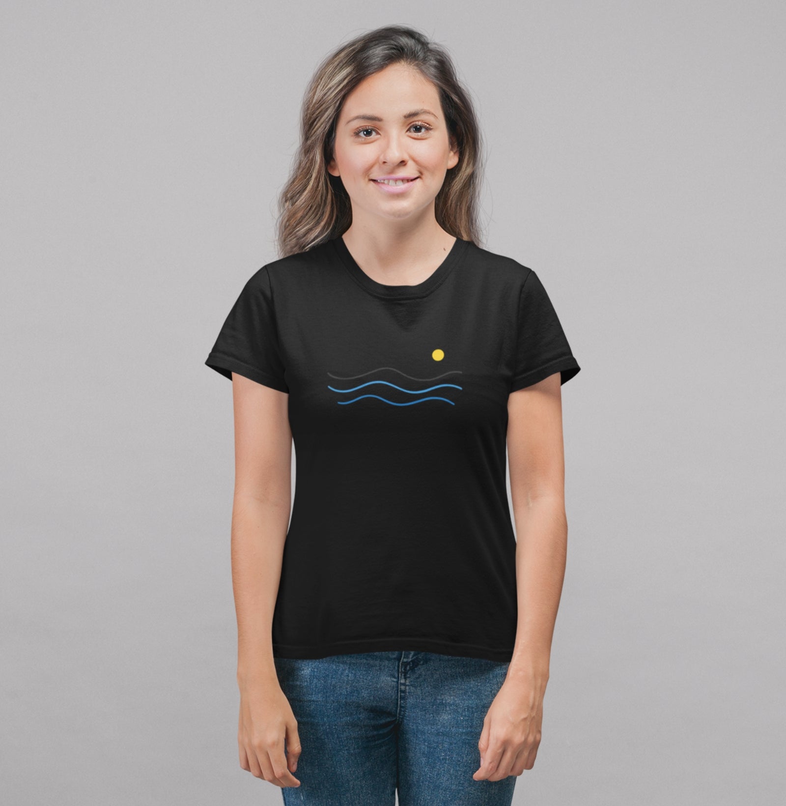 Camiseta preta Blue South da Latitude23 com design minimalista de ondas azuis e sol dourado, usada por mulher sorridente com jeans em fundo neutro.
