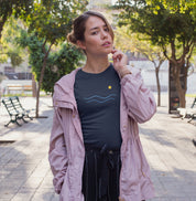 Camiseta azul marinho Blue South da Latitude23 com design minimalista de ondas azuis e sol dourado, usada por mulher em ambiente urbano com jaqueta rosa.