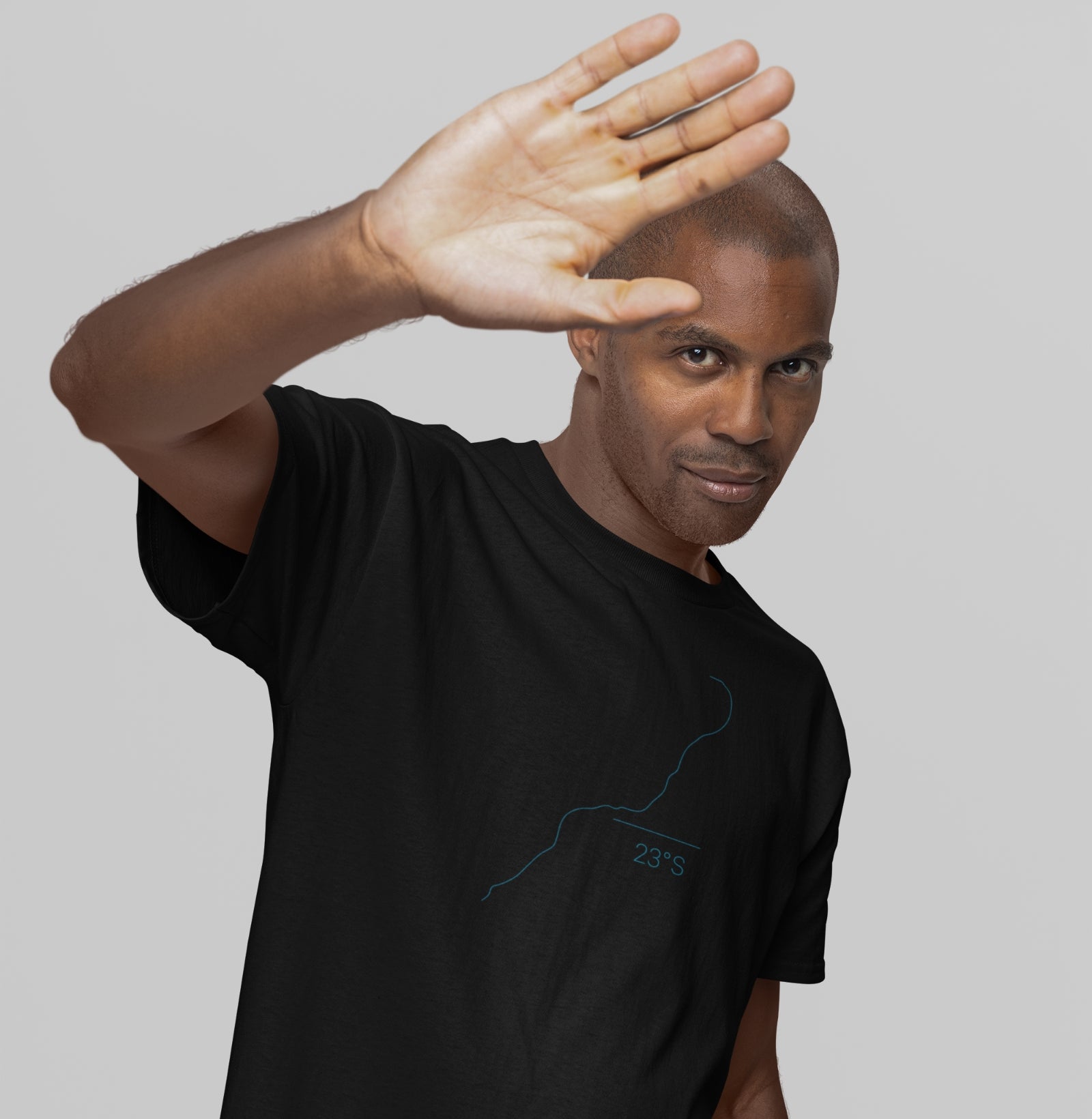 Camiseta preta Coastal Line da Latitude23 com design minimalista do contorno da costa e coordenada 23S, usada por homem em pose descontraída com a mão erguida.