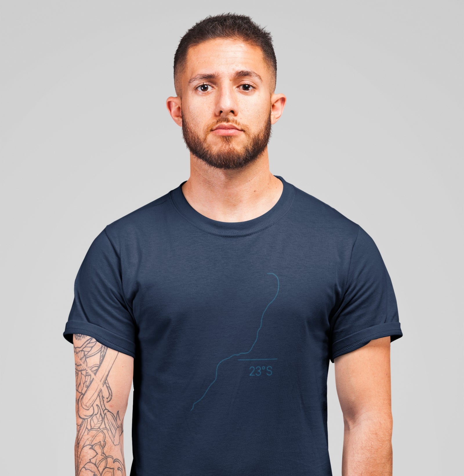 Camiseta azul marinho Coastal Line da Latitude23 com design minimalista do traçado da costa e coordenada 23S, usada por homem com tatuagem no braço esquerdo.