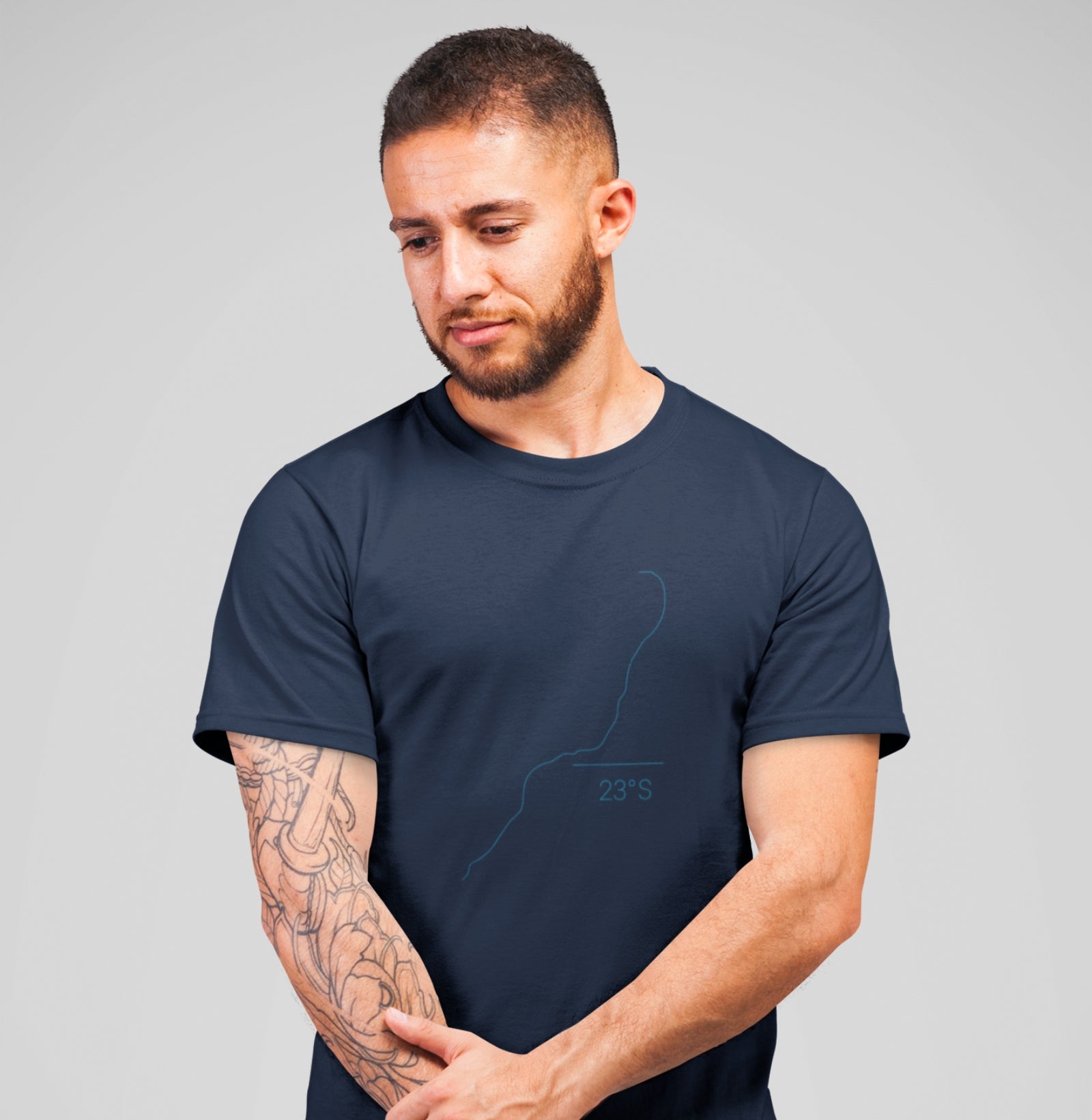 Camiseta azul marinho Coastal Line da Latitude23 com design minimalista da costa e coordenada 23S, usada por homem com tatuagem no braço em pose casual.