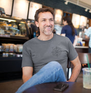 Homem usando a camiseta cinza Guiding Wind da Latitude23 em um café, mostrando a estampa de rosa dos ventos e o estilo náutico casual e sofisticado da marca.