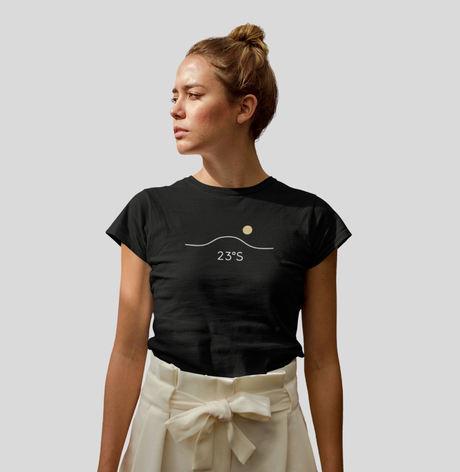Camiseta preta Horizon 23°S da Latitude23 com design minimalista de linha do horizonte, sol dourado e coordenada 23°S, usada por mulher de look elegante e contemporâneo.