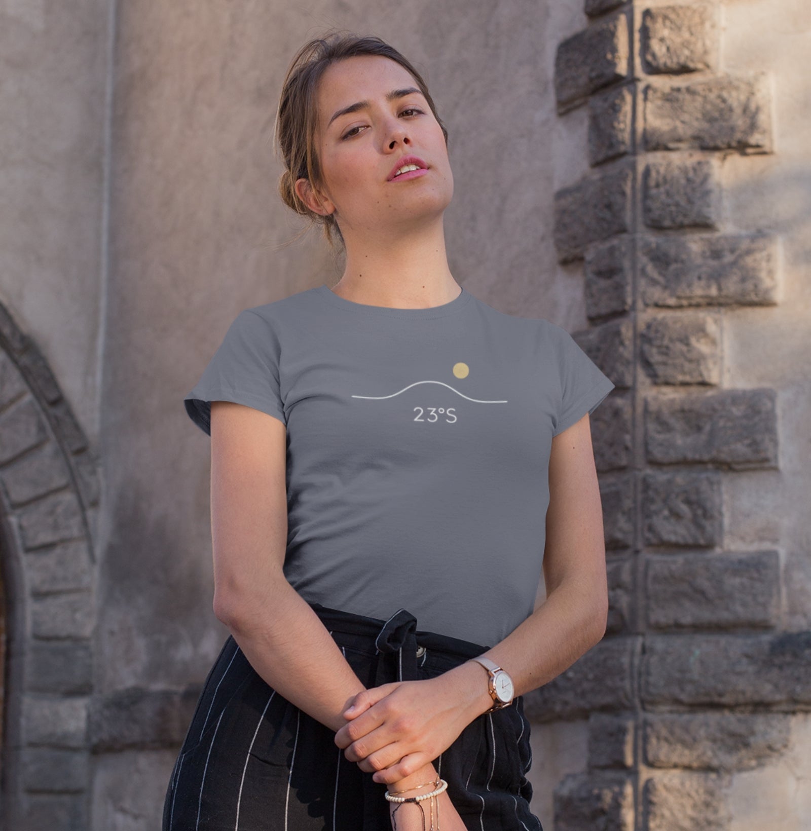 Camiseta cinza Horizon 23°S da Latitude23 com design minimalista de linha do horizonte, sol dourado e coordenada 23°S, usada por mulher em ambiente urbano iluminado.