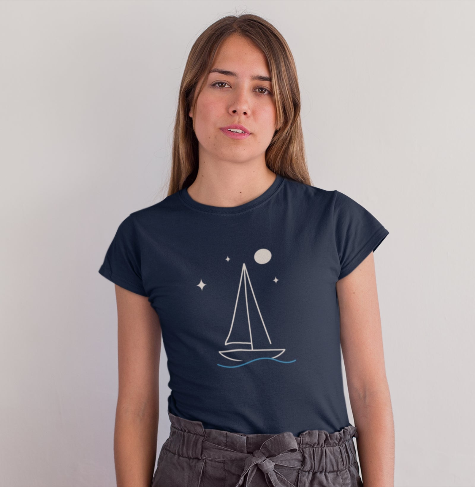 Mulher vestindo camiseta azul marinho Horizonte de Prata da Latitude23, com estampa minimalista de veleiro sob estrelas e lua, simbolizando serenidade e liberdade.
