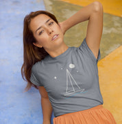 Mulher deitada usando camiseta cinza Horizonte de Prata da Latitude23, com estampa de veleiro sob a lua e estrelas, refletindo calma, mar e liberdade.