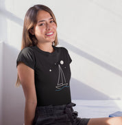 Mulher sorrindo com camiseta preta Horizonte de Prata da Latitude23, exibindo estampa minimalista de veleiro sob estrelas e lua, inspirada na calma do mar noturno.