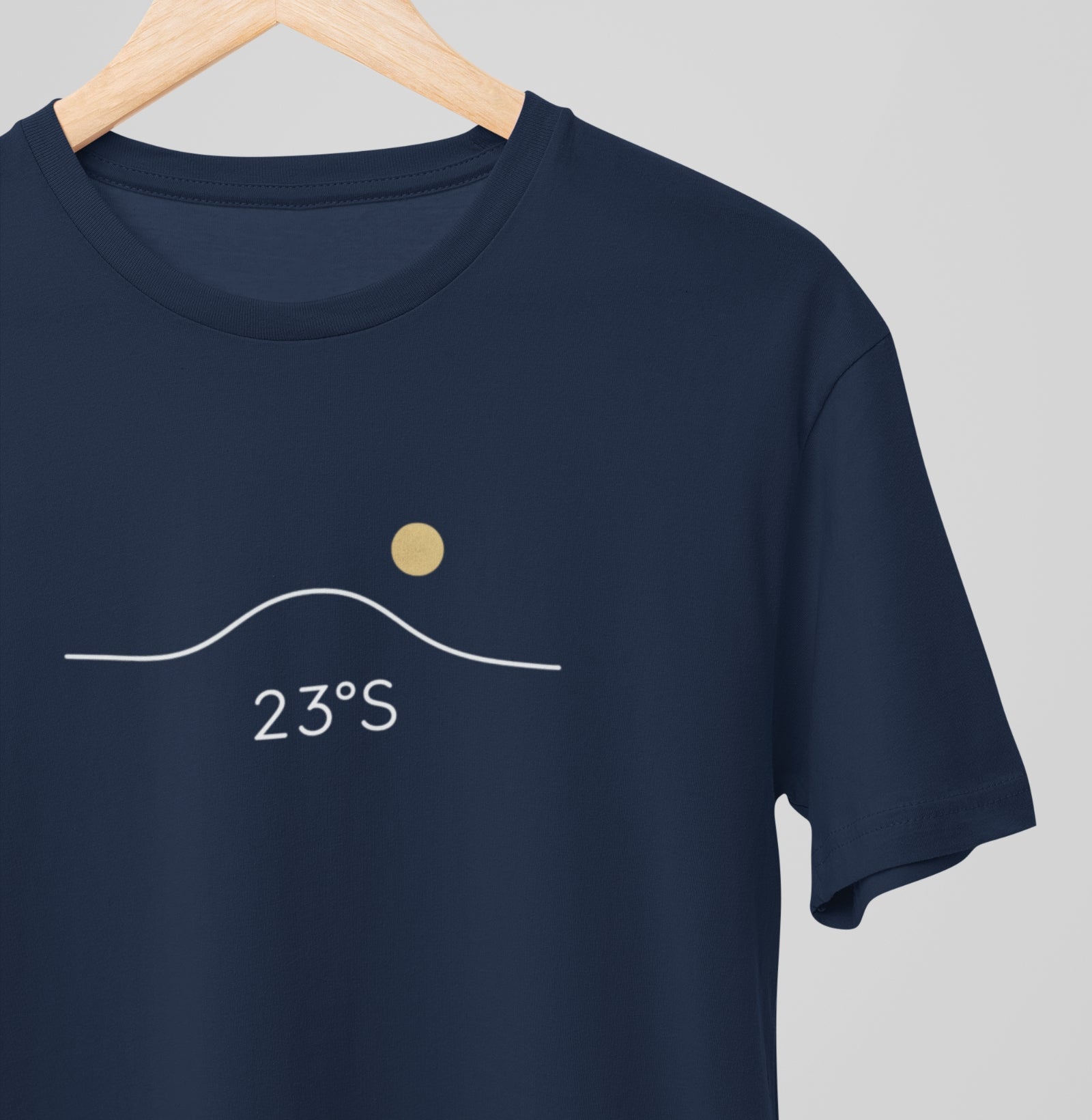Camiseta azul marinho Line Twenty-Three da Latitude23 pendurada em cabide, exibindo o design minimalista 23°S com sol dourado e traço contínuo inspirado no mar.