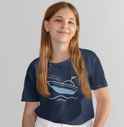 Menina usando camiseta azul marinho Open Horizon da Latitude23, com estampa de barco minimalista em azul e vermelho, transmitindo leveza e espírito marítimo.