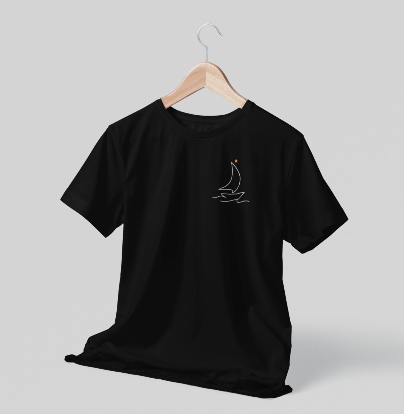 Camiseta preta Sea Ahead da Latitude23 pendurada em cabide, com design minimalista de veleiro em traço branco e ponto dourado, refletindo o estilo náutico elegante.