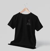 Camiseta preta Sea Ahead da Latitude23 pendurada em cabide, com design minimalista de veleiro em traço branco e ponto dourado, refletindo o estilo náutico elegante.