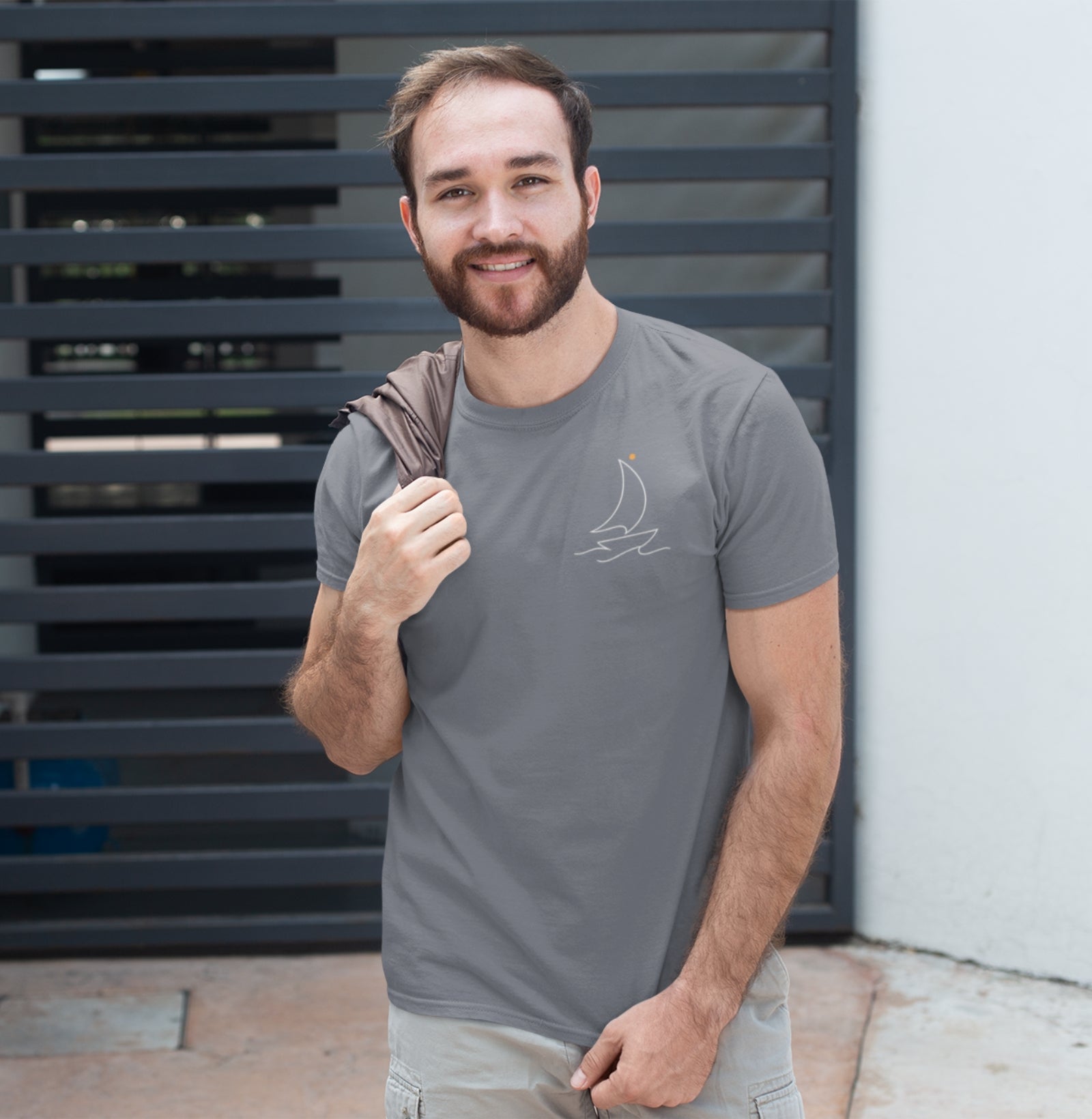Camiseta cinza Sea Ahead da Latitude23 com design minimalista de veleiro em traço branco e ponto dourado, usada por um homem sorridente em ambiente urbano casual.