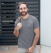 Camiseta cinza Sea Ahead da Latitude23 com design minimalista de veleiro em traço branco e ponto dourado, usada por um homem sorridente em ambiente urbano casual.