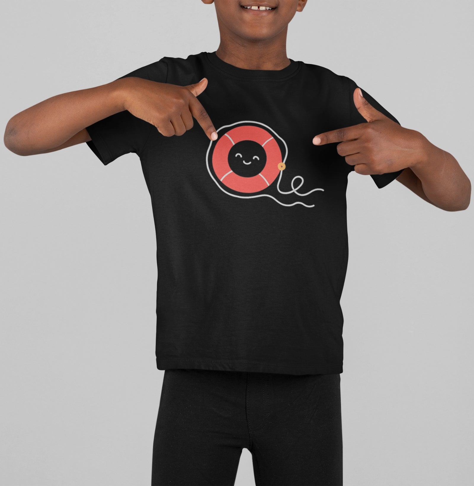 Menino sorrindo e apontando para a estampa da camiseta preta Sea Hugger da Latitude23, com boia vermelha e traços minimalistas inspirados no universo náutico.