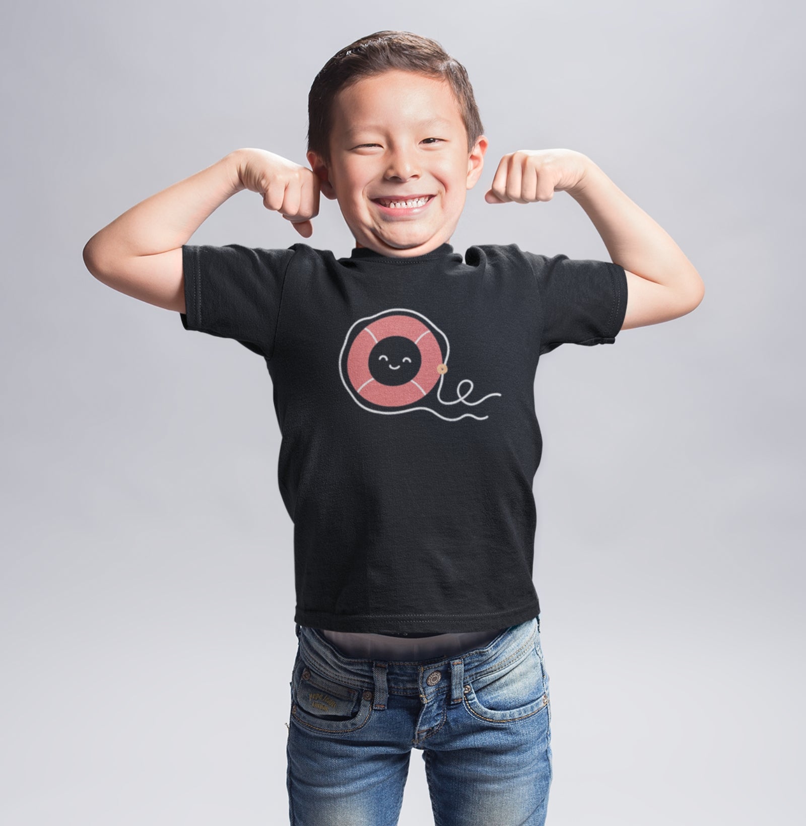 Menino sorrindo e mostrando os músculos com a camiseta preta Sea Hugger da Latitude23, que traz uma estampa divertida de boia vermelha com rosto sorridente.